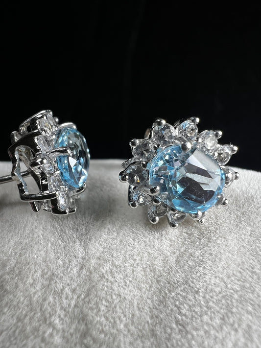 These sterling silver earrings showcase a captivating light blue lab-created topaz, elegantly framed by delicate white spinels. The combination highlights the topaz’s serene hue while adding subtle sparkle.