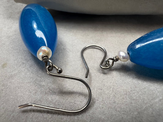 These earrings feature natural blue stones that captivate with their vibrant hue, elegantly complemented by delicate pearls. Crafted with sterling silver components, they combine quality materials and distinctive design.