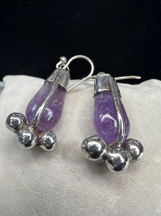 These vintage sterling silver drop earrings feature striking amethyst stones. Their distinctive design combines classic elegance with a bold, unique style, making them an exceptional accessory.
