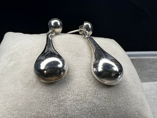 Pair of silver teardrop earrings on a white cushion with a dark background