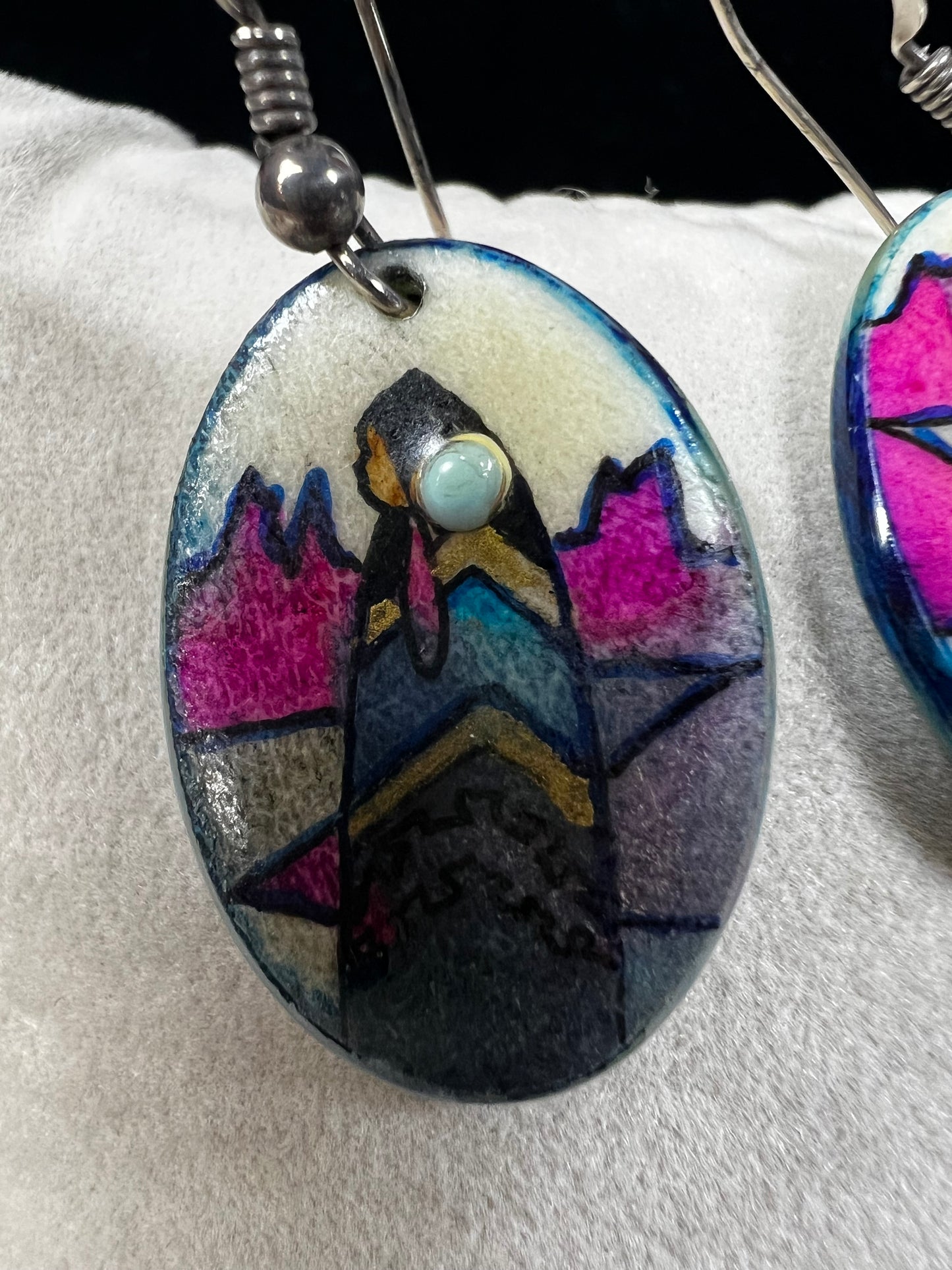 These vintage handmade earrings showcase a vibrant native scene on a lightweight material, expertly crafted to highlight intricate details and rich colors. They are completed with sterling silver hooks.