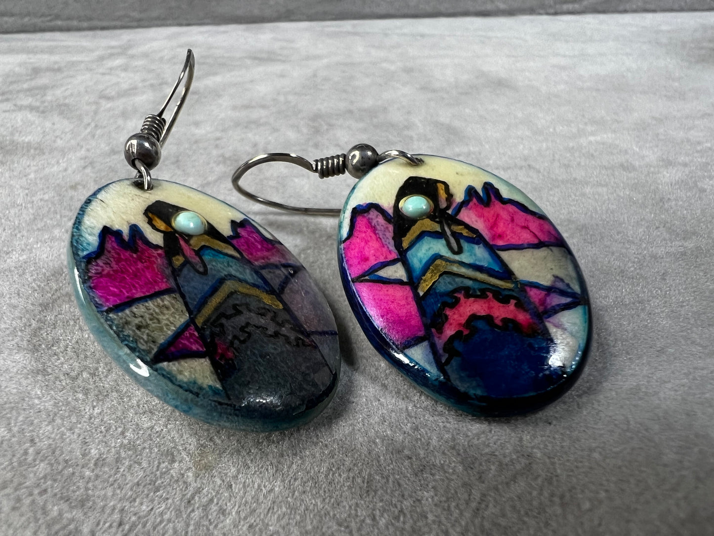 These vintage handmade earrings showcase a vibrant native scene on a lightweight material, expertly crafted to highlight intricate details and rich colors. They are completed with sterling silver hooks.
