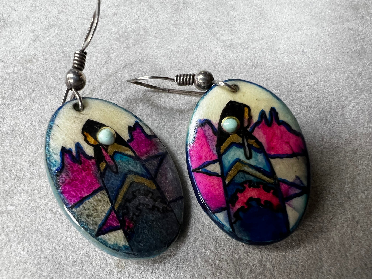 These vintage handmade earrings showcase a vibrant native scene on a lightweight material, expertly crafted to highlight intricate details and rich colors. They are completed with sterling silver hooks.