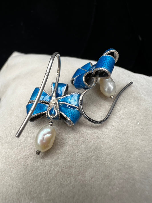 These sterling silver earrings feature expertly crafted blue enamel bows, each accented with a delicate pearl drop. The combination of lustrous pearls and vibrant enamel will add a refined touch to any outfit.