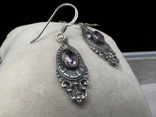 These sterling silver dangle earrings showcase an intricate design centered around a vibrant amethyst gemstone. The rich purple hue of the amethyst will add a refined splash of color to your outfit.