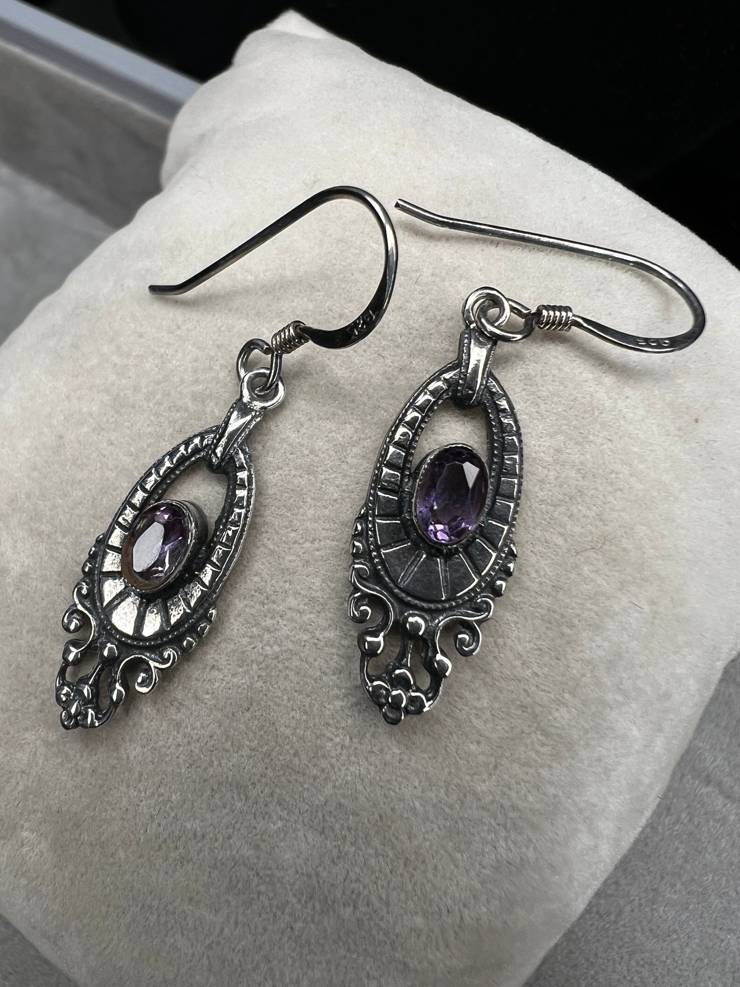 These sterling silver dangle earrings showcase an intricate design centered around a vibrant amethyst gemstone. The rich purple hue of the amethyst will add a refined splash of color to your outfit.