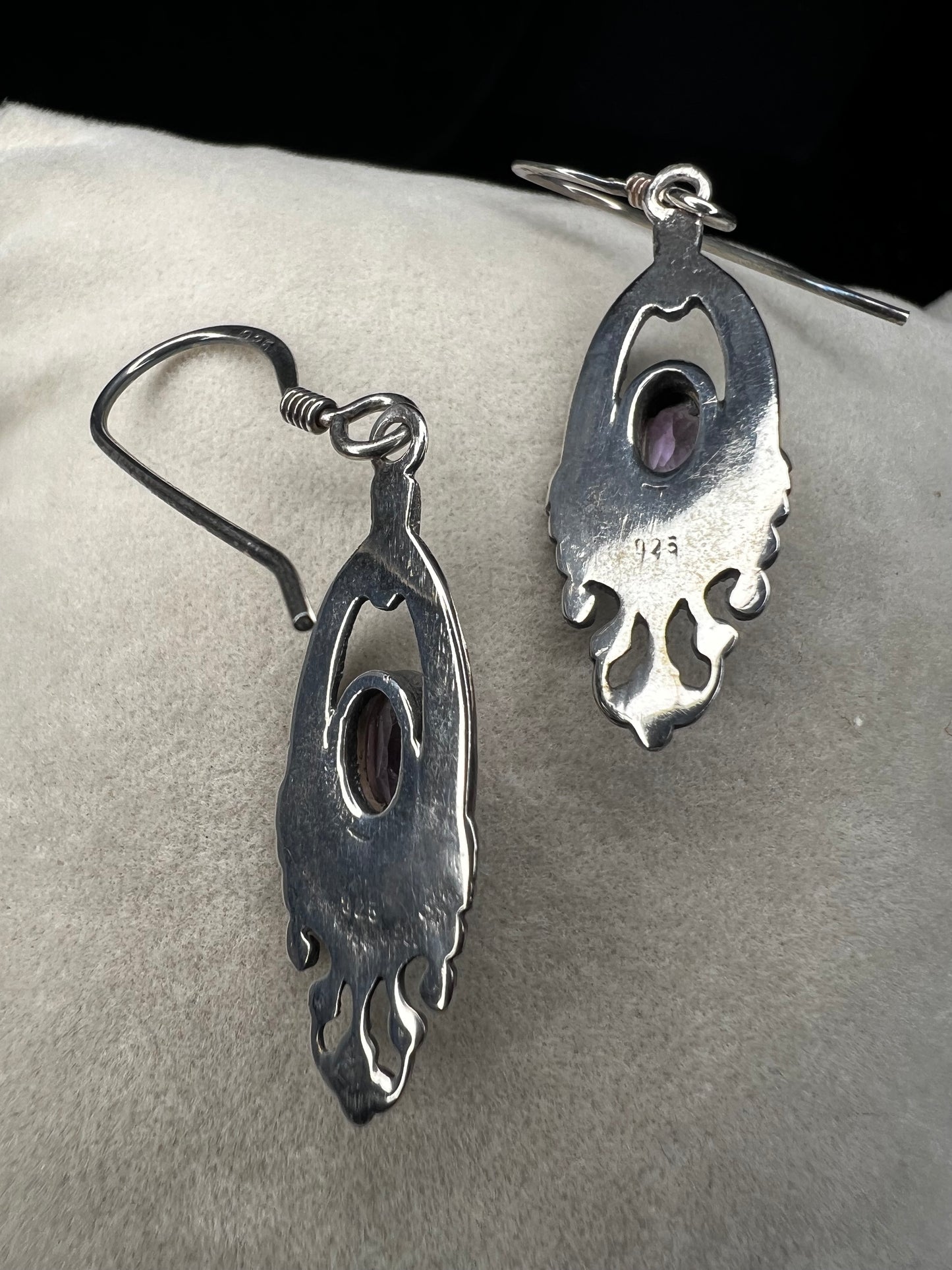 These sterling silver dangle earrings showcase an intricate design centered around a vibrant amethyst gemstone. The rich purple hue of the amethyst will add a refined splash of color to your outfit.