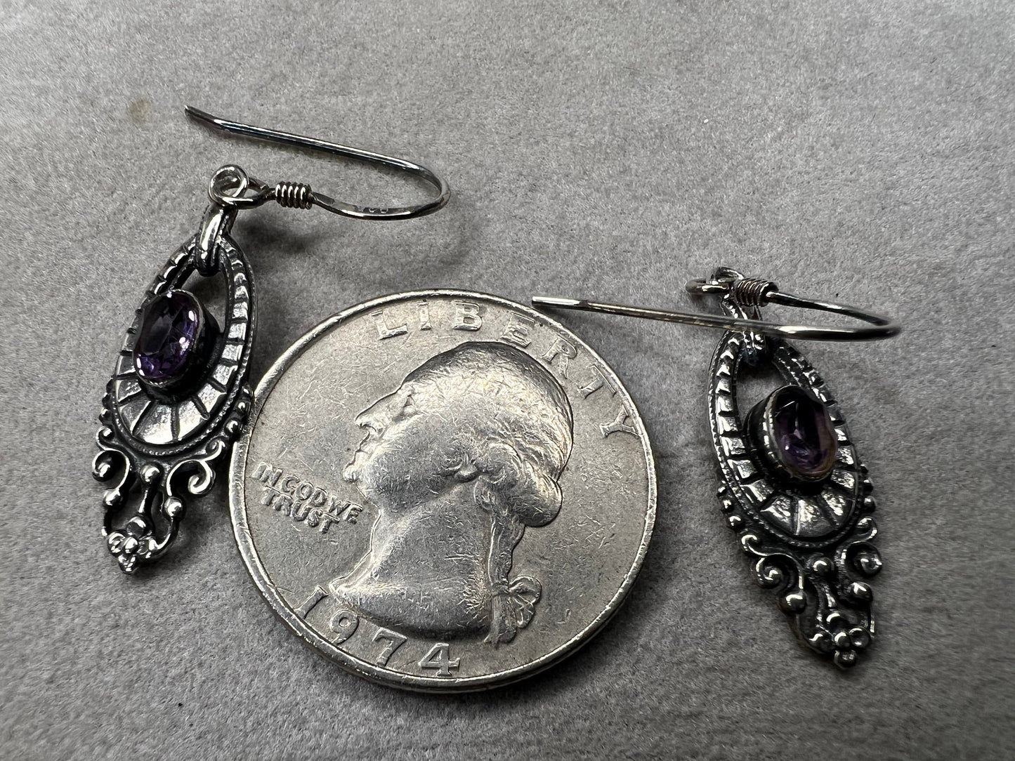 These sterling silver dangle earrings showcase an intricate design centered around a vibrant amethyst gemstone. The rich purple hue of the amethyst will add a refined splash of color to your outfit.