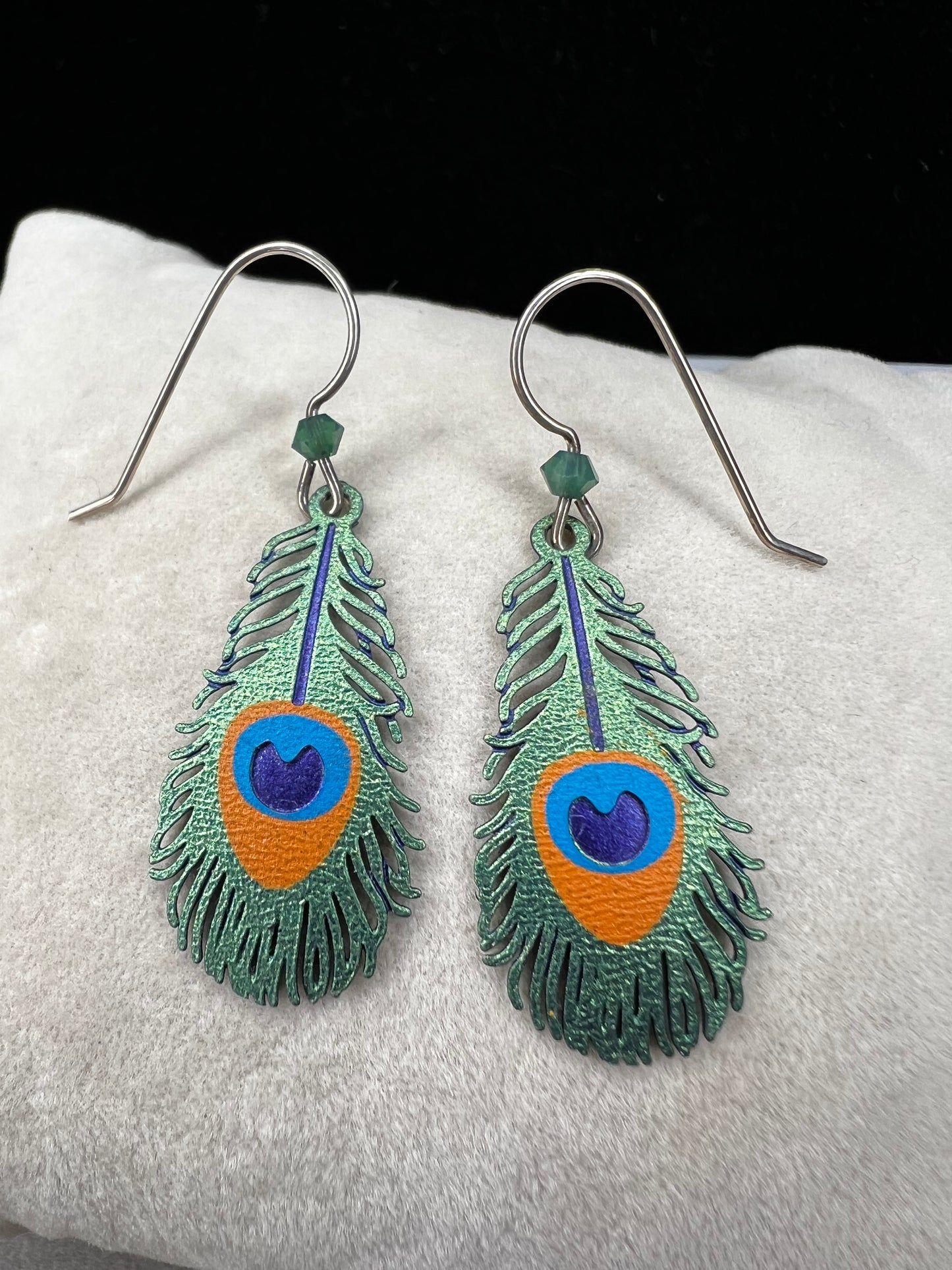 These sterling silver earrings showcase a unique design inspired by peacock feathers, enhanced with vibrant enamel detailing.