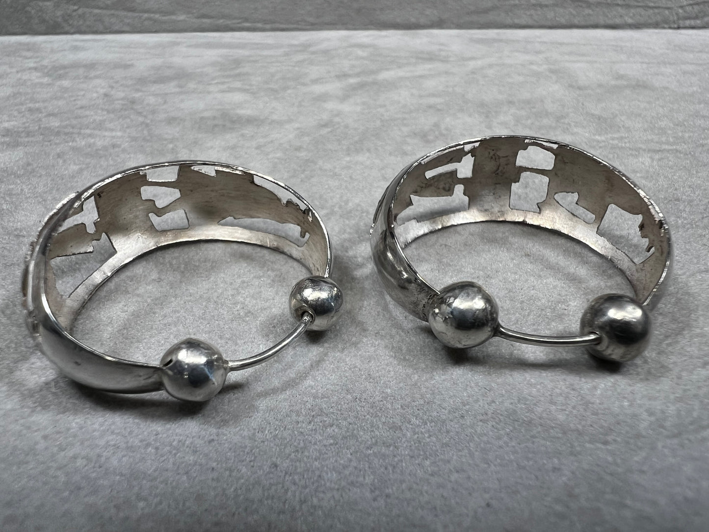 These vintage sterling silver hoop earrings showcase intricate cut-out silhouettes, blending classic design with artistic detail. Perfect for adding a subtle yet distinctive touch to any outfit.