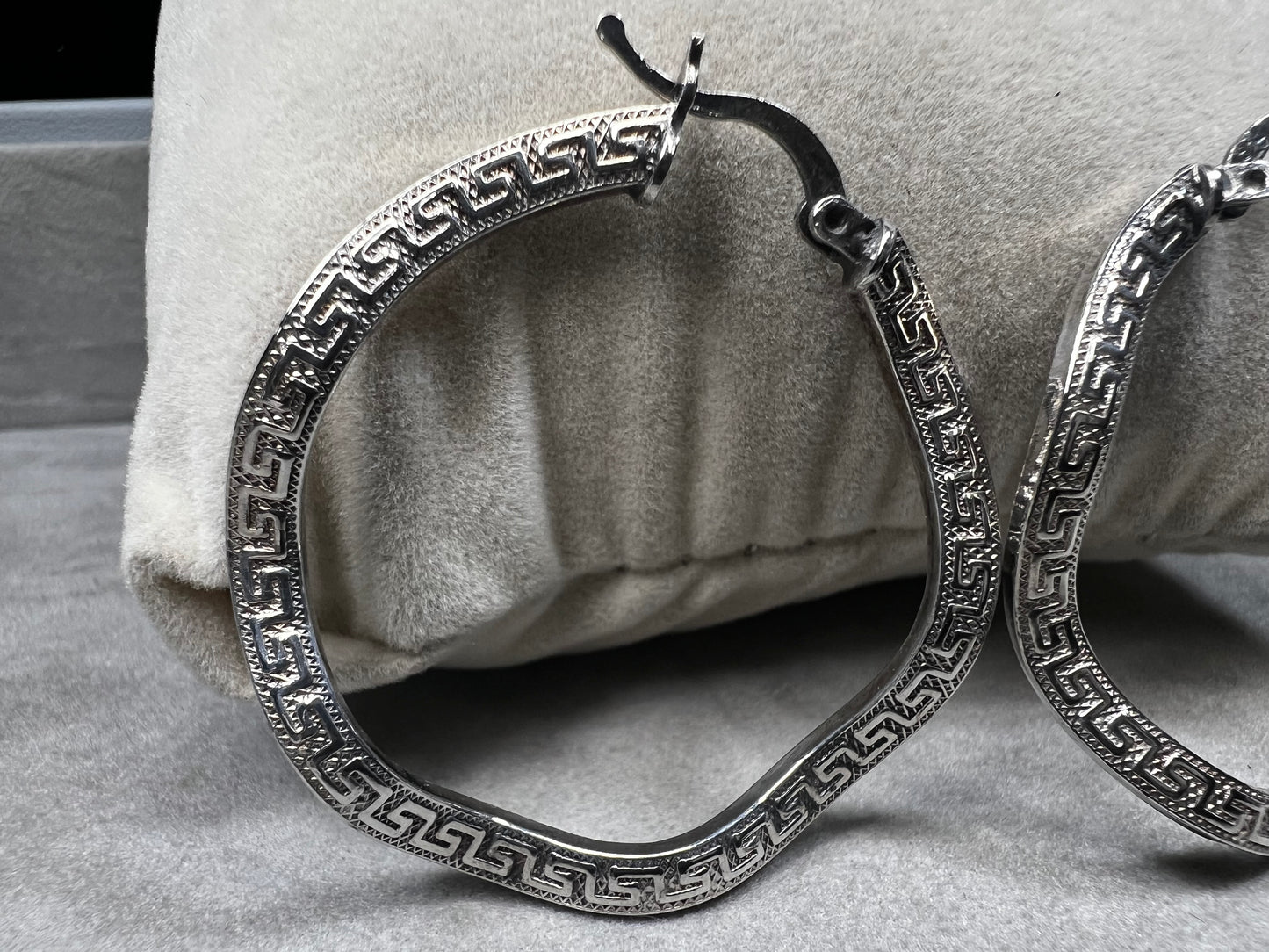 These sterling silver hoop earrings showcase a wavy design enhanced by a timeless Greek key pattern. They combine classic motifs with modern elegance, making them a versatile accessory.