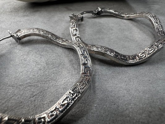 These sterling silver hoop earrings showcase a wavy design enhanced by a timeless Greek key pattern. They combine classic motifs with modern elegance, making them a versatile accessory.