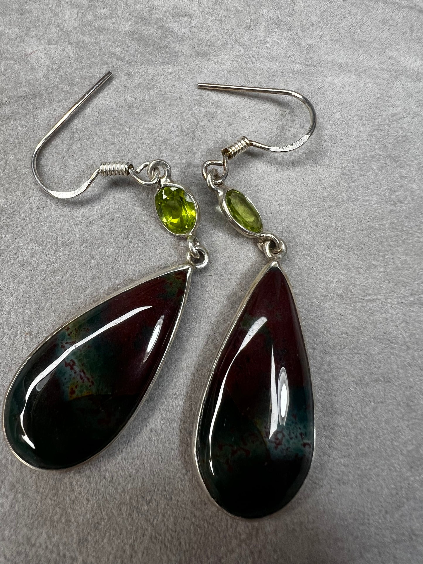 These sterling silver earrings feature a large teardrop-shaped bloodstone paired with a bright peridot, creating a distinctive and elegant look.