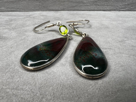 These sterling silver earrings feature a large teardrop-shaped bloodstone paired with a bright peridot, creating a distinctive and elegant look.