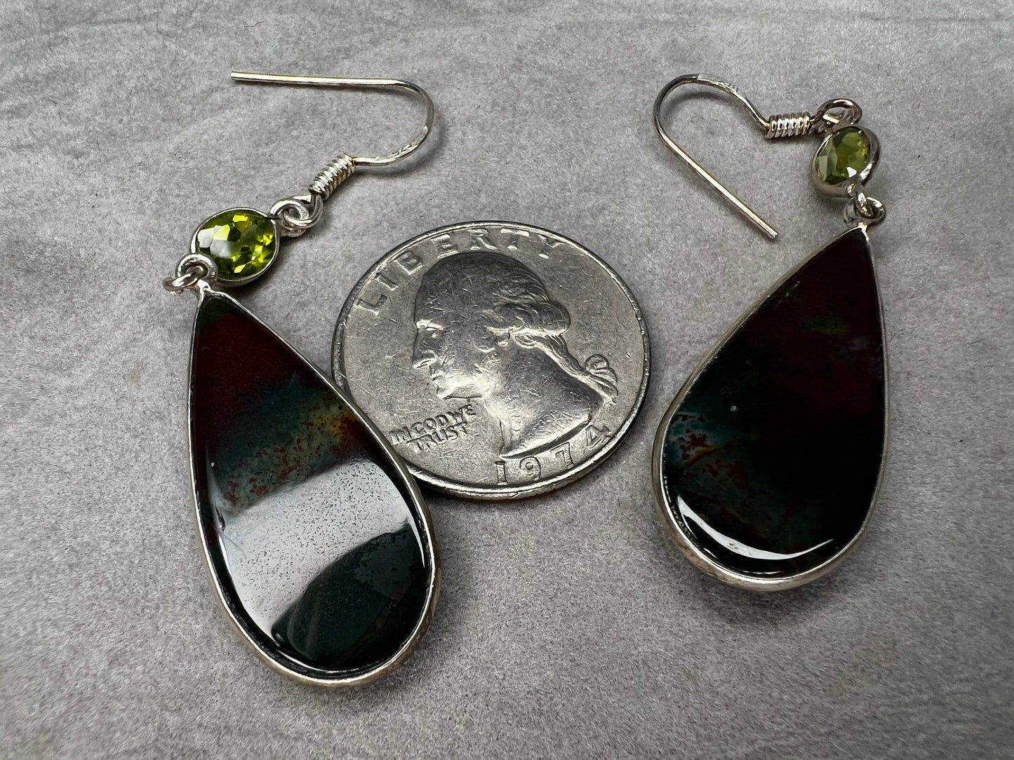 These sterling silver earrings feature a large teardrop-shaped bloodstone paired with a bright peridot, creating a distinctive and elegant look.