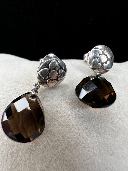 These sterling silver drop earrings feature a delicate flower design button paired with a faceted smoky quartz pendant. Their elegant combination will add a touch of natural beauty and subtle sophistication to your outfit.