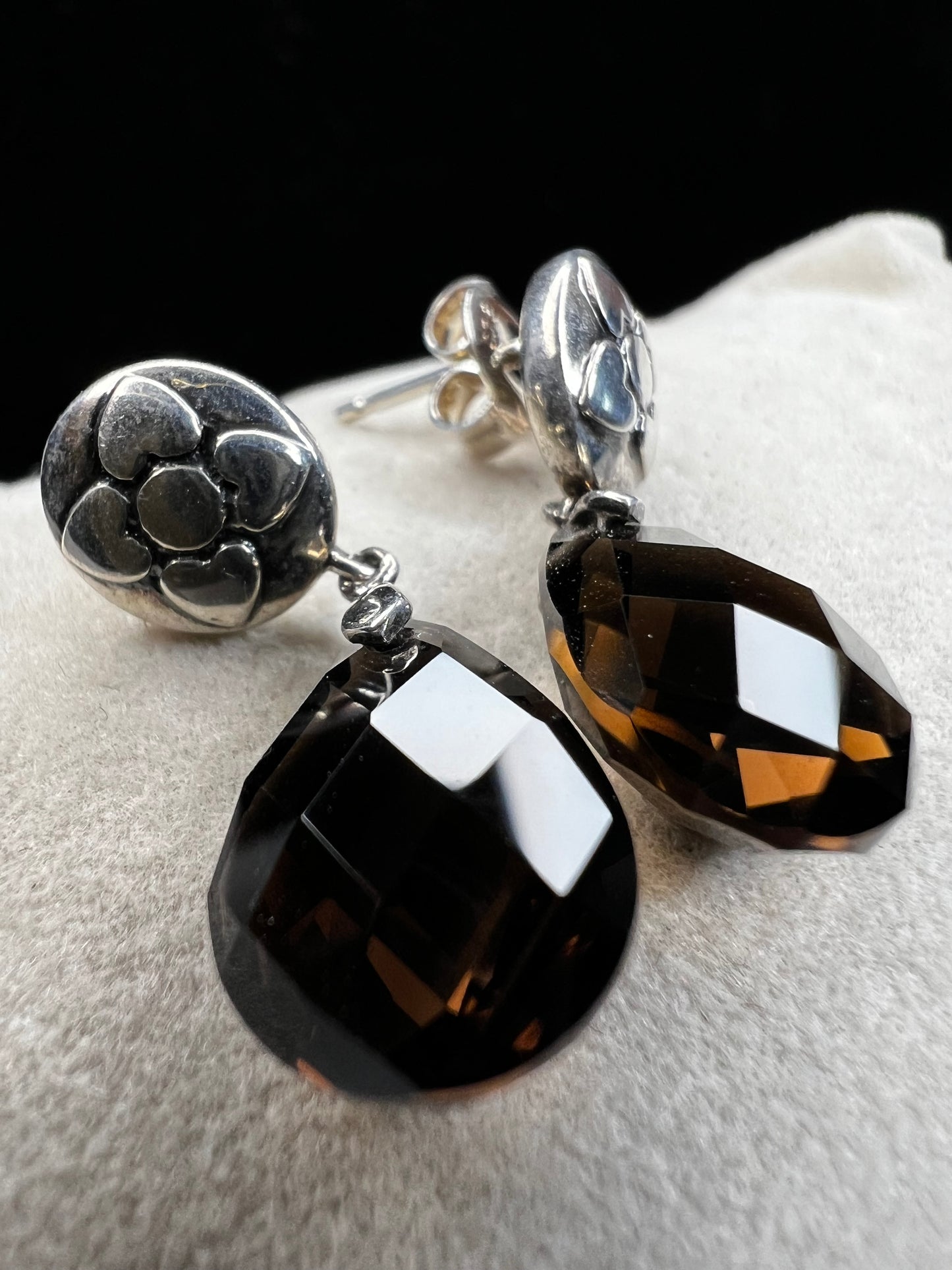 These sterling silver drop earrings feature a delicate flower design button paired with a faceted smoky quartz pendant. Their elegant combination will add a touch of natural beauty and subtle sophistication to your outfit.