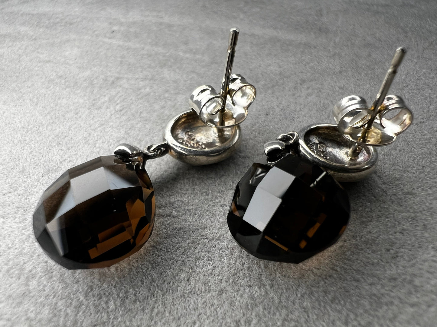 These sterling silver drop earrings feature a delicate flower design button paired with a faceted smoky quartz pendant. Their elegant combination will add a touch of natural beauty and subtle sophistication to your outfit.