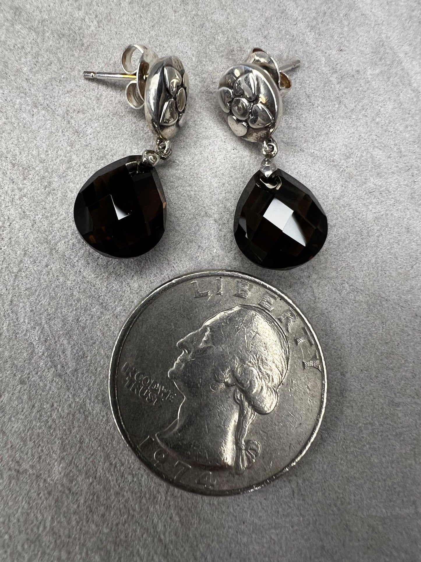 These sterling silver drop earrings feature a delicate flower design button paired with a faceted smoky quartz pendant. Their elegant combination will add a touch of natural beauty and subtle sophistication to your outfit.