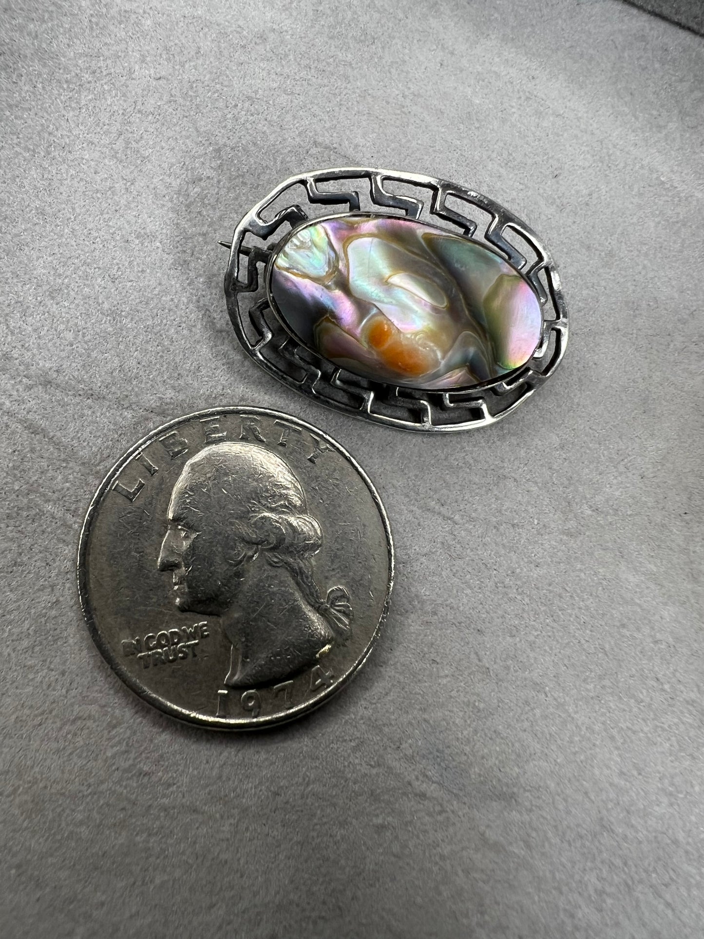 This vintage brooch showcases a tall abalone shell beautifully set within a sterling silver frame that features a classic Greek key design. Its elegant combination of natural iridescence and timeless pattern makes it a standout accessory that adds refined charm to any ensemble.