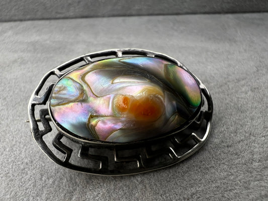 This vintage brooch showcases a tall abalone shell beautifully set within a sterling silver frame that features a classic Greek key design. Its elegant combination of natural iridescence and timeless pattern makes it a standout accessory that adds refined charm to any ensemble.