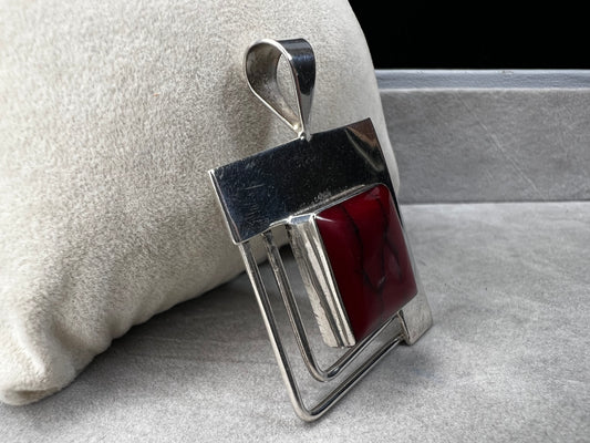 This striking sterling silver pendant features a bold blood red faux stone, designed to stand out beautifully with larger silver chains. Handcrafted in Mexico, it combines unique artistry with timeless elegance, making it a perfect statement piece to complement your collection.