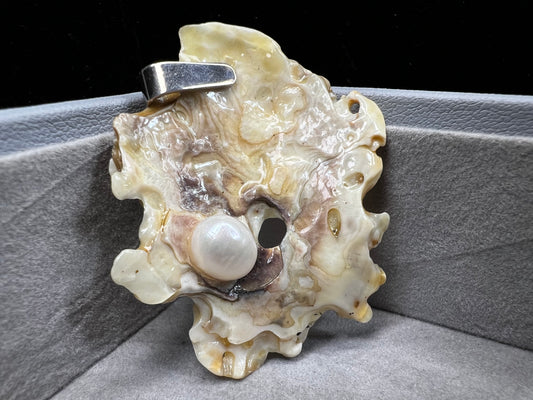This pendant is crafted from a natural oyster and pearl, complemented by a sterling silver bail for a refined finish. Its unique design offers a special touch.