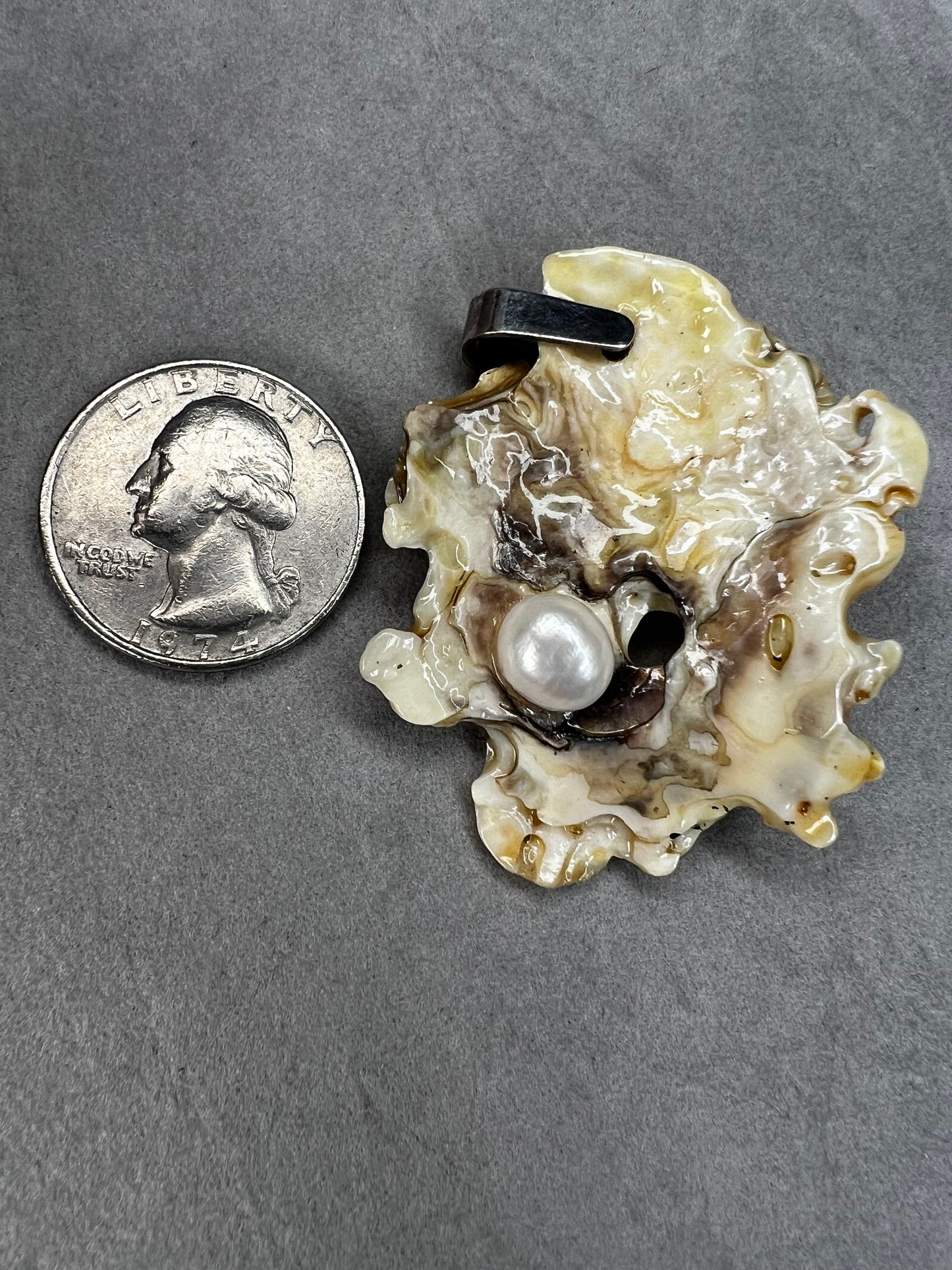 This pendant is crafted from a natural oyster and pearl, complemented by a sterling silver bail for a refined finish. Its unique design offers a special touch.