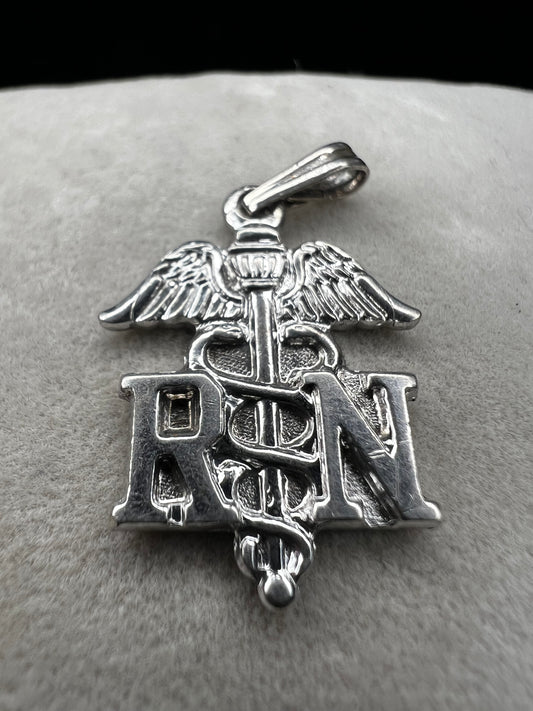 Celebrate the dedication of nurses with this vintage sterling silver RN pendant. It serves as a meaningful symbol of commitment and care. Perfect for everyday wear or as a thoughtful gift.