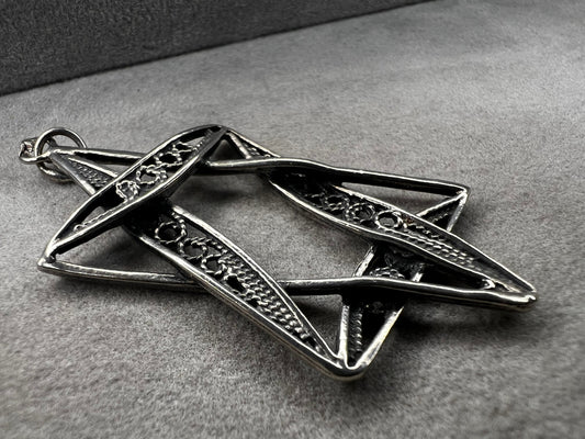 This sterling silver Star of David pendant, measuring nearly 2 inches, showcases intricate filigree craftsmanship. Its delicate design highlights expert artistry, making it a meaningful and elegant accessory.