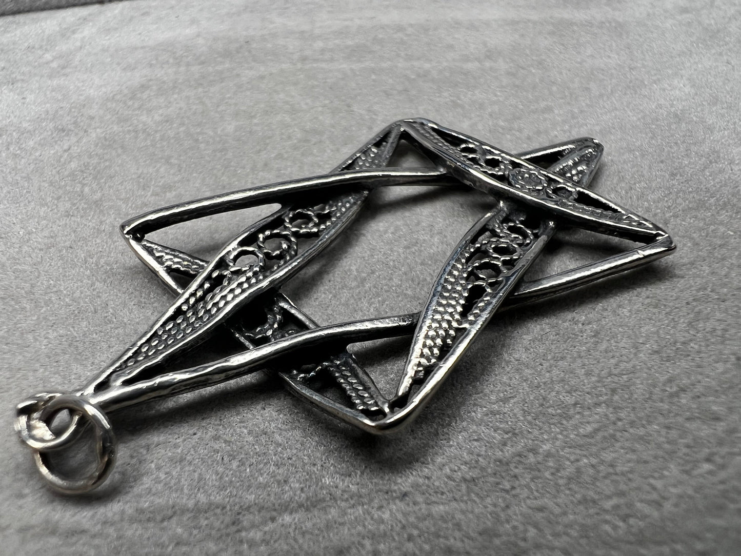 This sterling silver Star of David pendant, measuring nearly 2 inches, showcases intricate filigree craftsmanship. Its delicate design highlights expert artistry, making it a meaningful and elegant accessory.