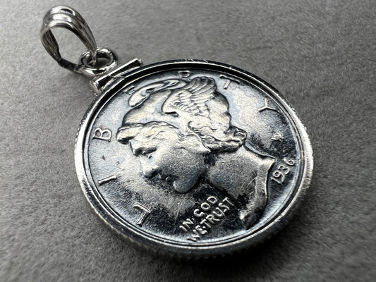This pendant features a genuine 1936 silver Liberty Head dime, elegantly framed in sterling silver with a matching bail. It is a timeless accessory that combines historical charm with refined craftsmanship.