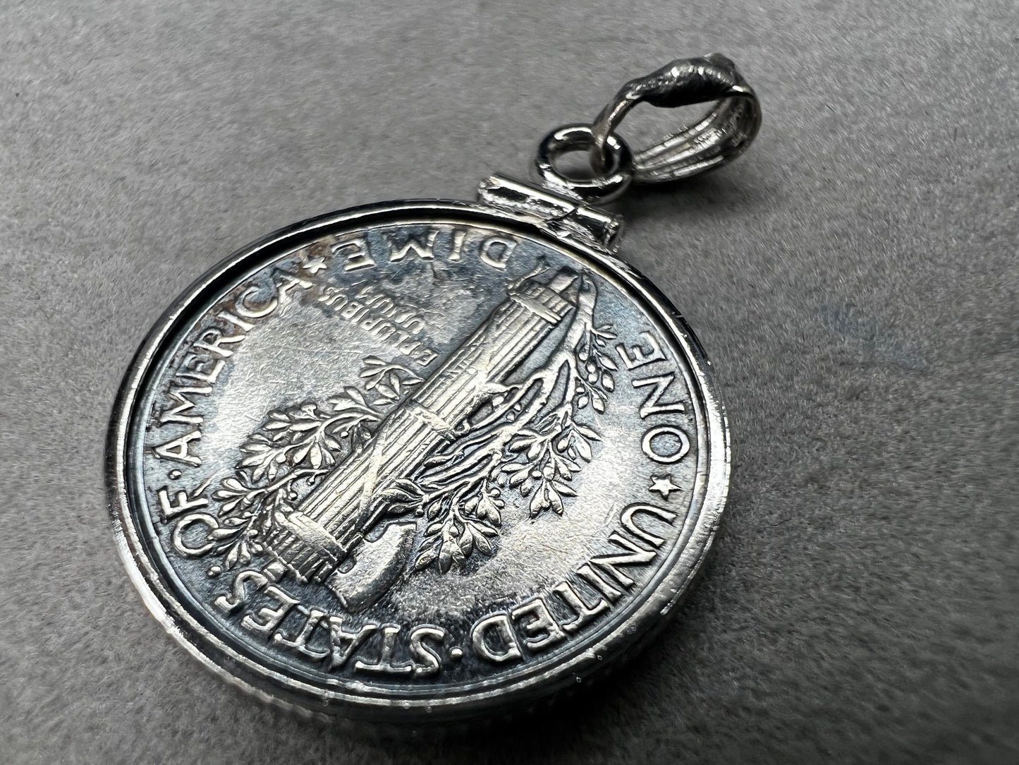 This pendant features a genuine 1936 silver Liberty Head dime, elegantly framed in sterling silver with a matching bail. It is a timeless accessory that combines historical charm with refined craftsmanship.