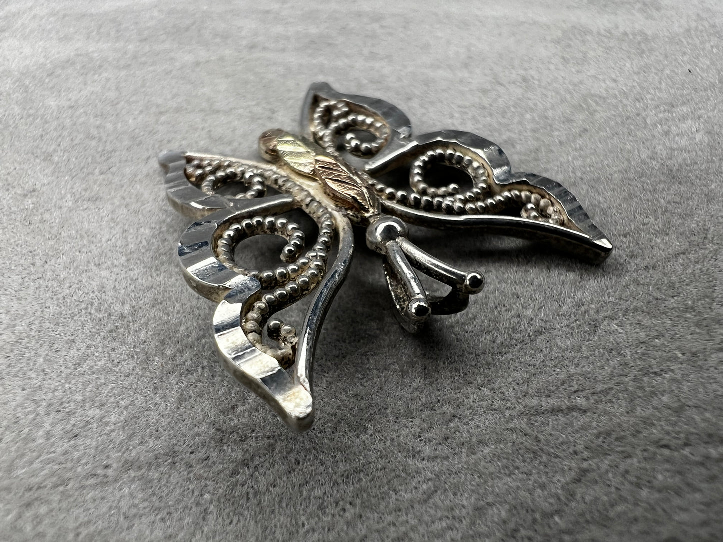 This vintage butterfly pendant combines the timeless elegance of sterling silver with the rich warmth of 12 karat gold. Signed C. Co., this Black Hills Gold piece is perfect for those who appreciate classic craftsmanship with a touch of sophistication.