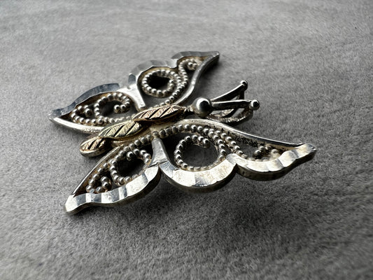 This vintage butterfly pendant combines the timeless elegance of sterling silver with the rich warmth of 12 karat gold. Signed C. Co., this Black Hills Gold piece is perfect for those who appreciate classic craftsmanship with a touch of sophistication.