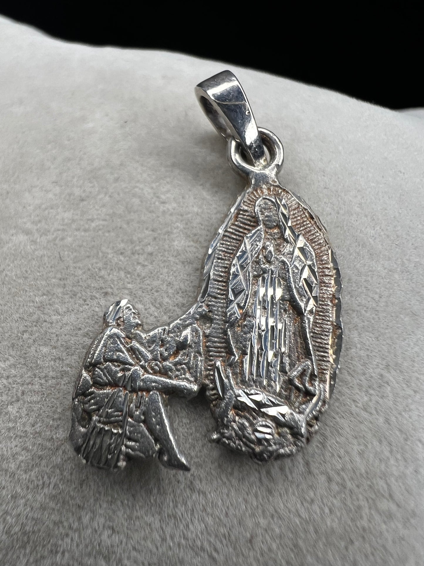 Crafted from sterling silver, this pendant shows a figure kneeling before another, suggestive of a religious deity. This piece is detailed with diamond cuts to catch the light.