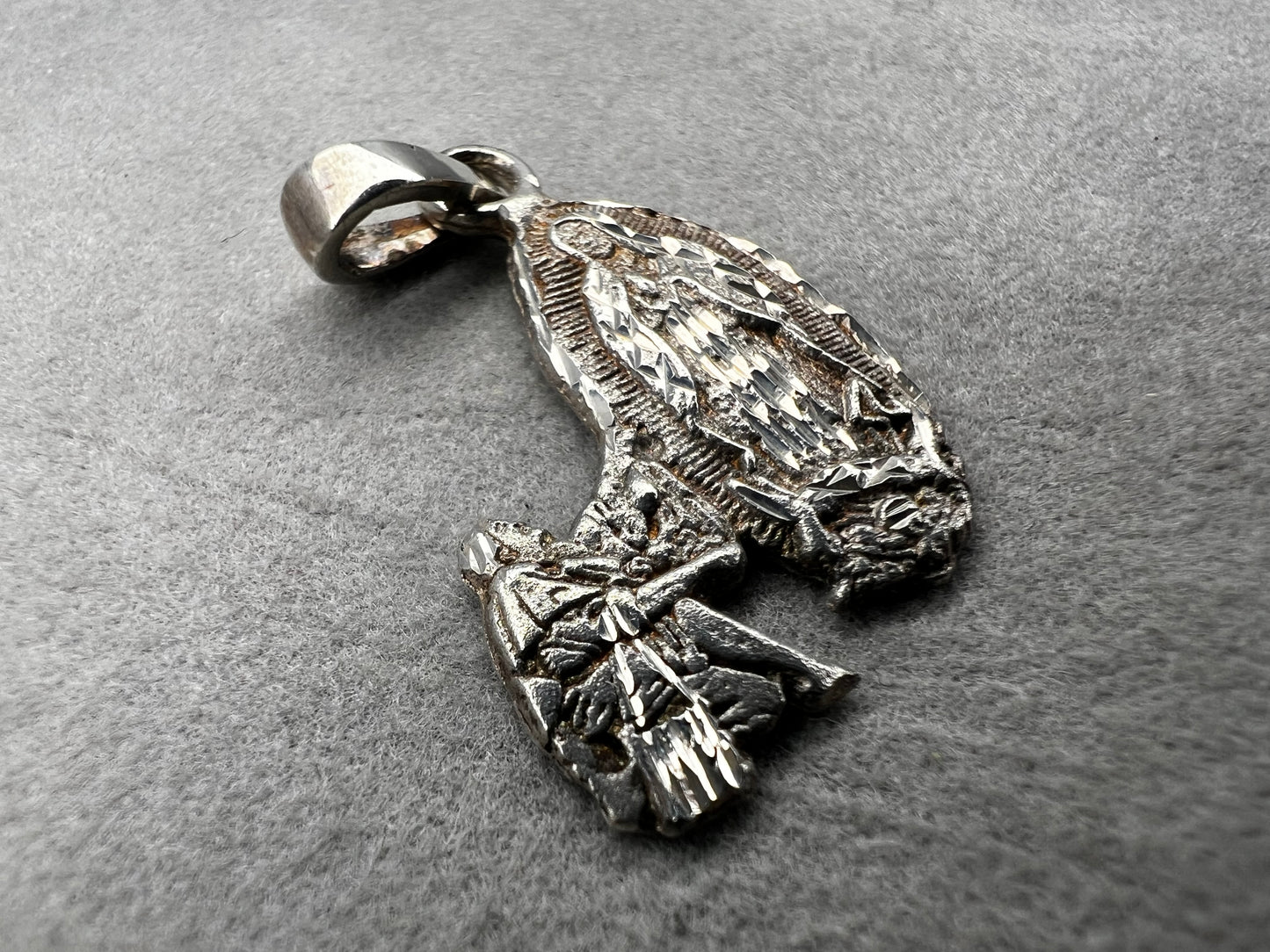 Crafted from sterling silver, this pendant shows a figure kneeling before another, suggestive of a religious deity. This piece is detailed with diamond cuts to catch the light.