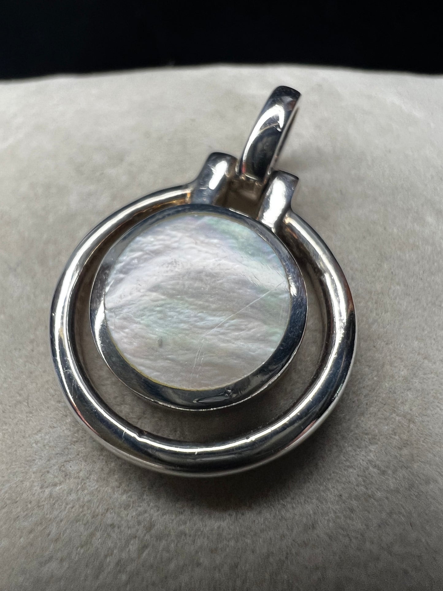 This sterling silver and mother of pearl pendant features a seamless design where the outer ring and bail are crafted as a single unit. The circular shape highlights the natural iridescence of the mother of pearl.