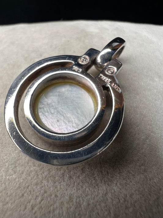 This sterling silver and mother of pearl pendant features a seamless design where the outer ring and bail are crafted as a single unit. The circular shape highlights the natural iridescence of the mother of pearl.