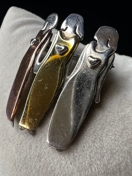 Signed "Far Fetched," this sterling silver pin features three women side by side, each wearing a different colored dress accented in brass, copper, and silver. A heartfelt design, it symbolizes friendship, sisterhood, and unity.