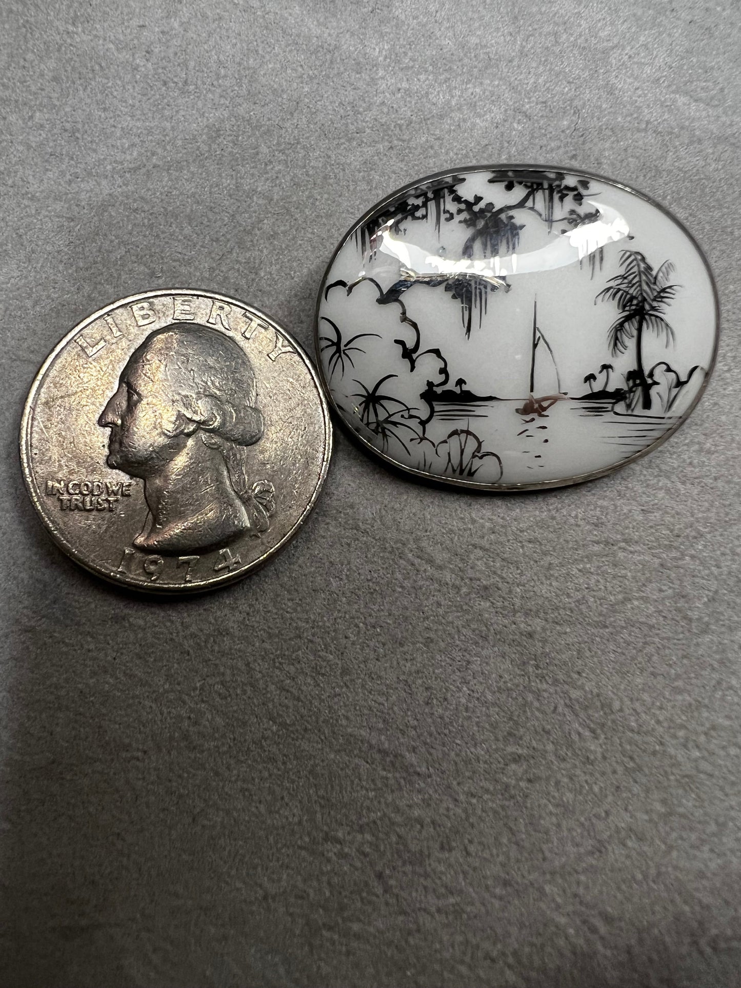 This vintage brooch is an original “cameona” by Florida artist Olive Commons, featuring a hand-painted porcelain scene of a sailboat and palms in her signature black linework with metallic accents. Commons coined the term cameona for these miniature painted landscapes, which became cherished Florida souvenirs and remain highly collectible today.