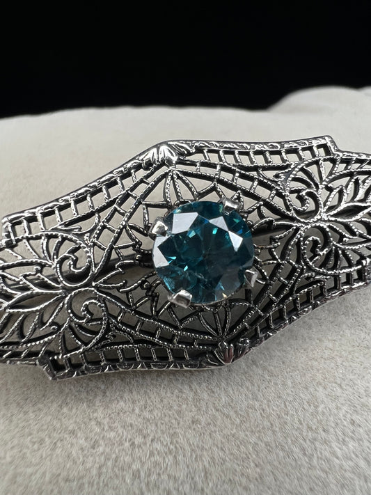 This antique filigree brooch features a beautiful blue topaz set in sterling silver, signed with a distinctive "K." Measuring 1.5 inches, it offers a delicate and elegant touch to any jewelry collection. Perfect for adding a vintage charm to your style.