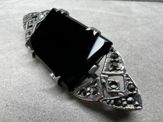 This vintage sterling silver brooch showcases a striking large rectangular onyx stone, beautifully complemented by marcasite accents on both openwork ends. Perfect for those who appreciate vintage charm and refined style.