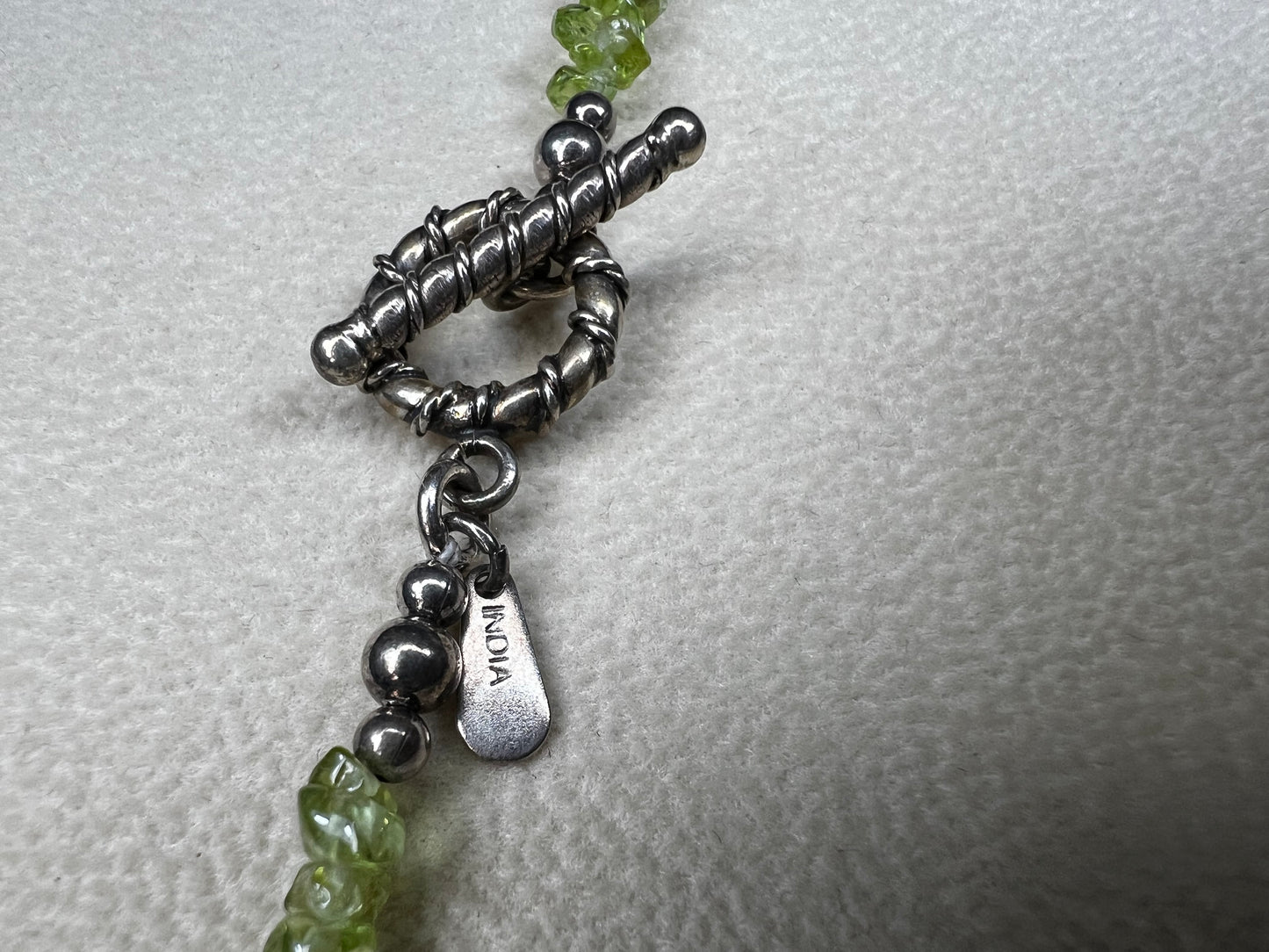 This 36-inch necklace features natural peridot chips expertly strung and paired with sterling silver components. Its vibrant green hues bring a refreshing touch, while sterling silver ensures durability and elegance. Made in India.