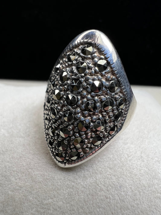 This striking vintage ring makes a bold statement with its wide, shield-shaped design. Crafted from sterling silver, the piece is beautifully set with glittering faceted marcasite stones, creating a dramatic sparkle that catches the light from every angle.