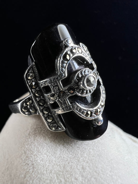 This striking vintage sterling silver ring features a polished black onyx cabochon accented with sparkling marcasite. Designed in an Art Deco revival style, this bold piece blends timeless elegance with dramatic flair.