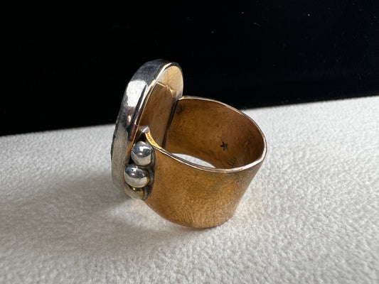 This ring by Loving Anvil features a dendritic limestone cabochon, which displays striking fern-like black inclusions that resemble a natural landscape. The stone is set in sterling silver against a brass band with a thin overlay of gold.