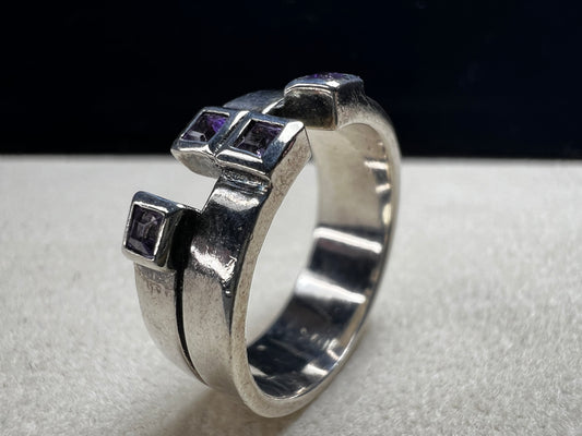 This sterling silver ring features a wide band expertly designed to resemble two distinct bands, creating a unique and sophisticated aesthetic. Adorned with vibrant amethyst stones, it offers expert craftsmanship and a refined look.