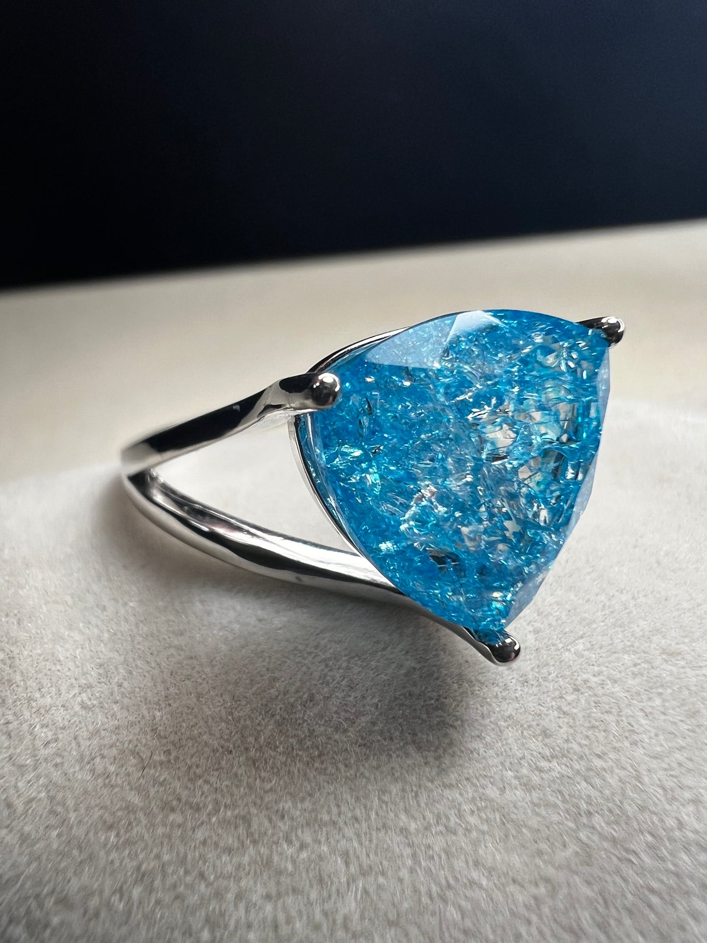 This sterling silver ring showcases a large, blue trilliant cut crackled quartz, creating a captivating centerpiece. Perfect for adding a touch of elegance and distinctiveness to any outfit.