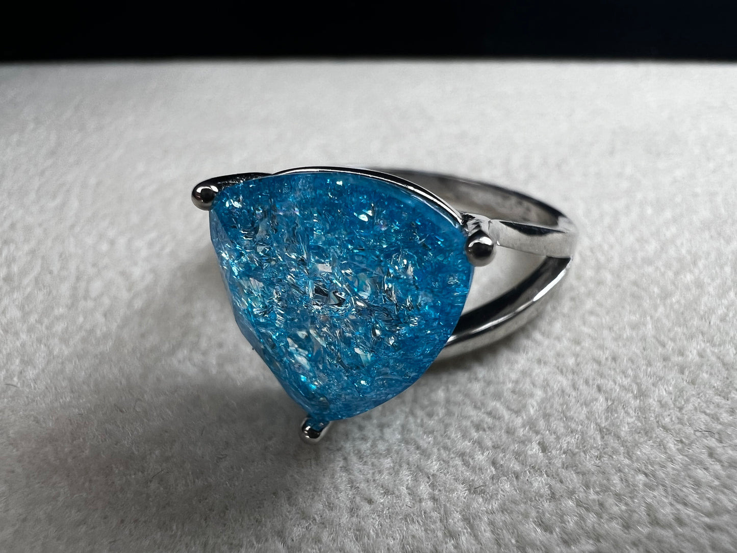 This sterling silver ring showcases a large, blue trilliant cut crackled quartz, creating a captivating centerpiece. Perfect for adding a touch of elegance and distinctiveness to any outfit.